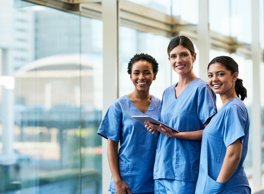 Three healthcare professionals in scrubs standing together in a hospital corridor