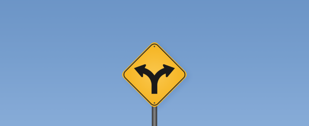 A yellow diamond road sign with a two-way fork arrow, mounted on a post against a clear blue sky.