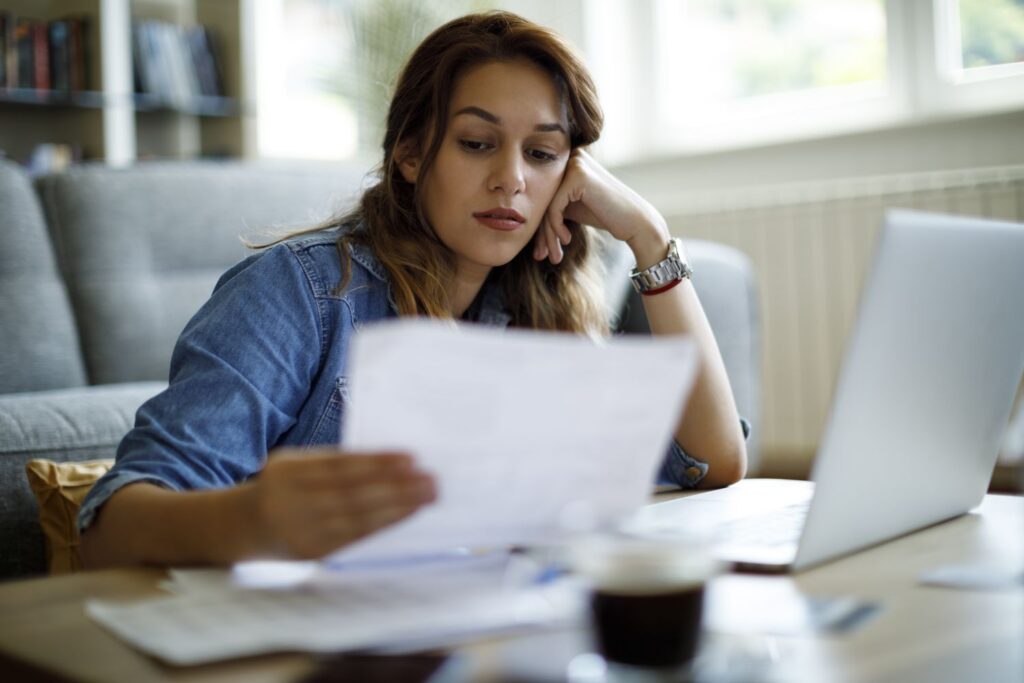 A borrower at a home table reading a loan statement beside a laptop while comparing the Repayment Assistance Plan and Income-Based Repayment.