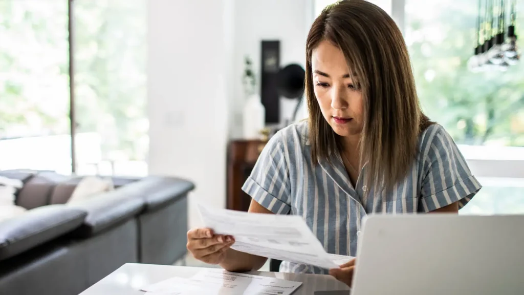 A borrower at a home table reading a statement beside an open laptop while working out the tax owed on forgiven student loan debt.