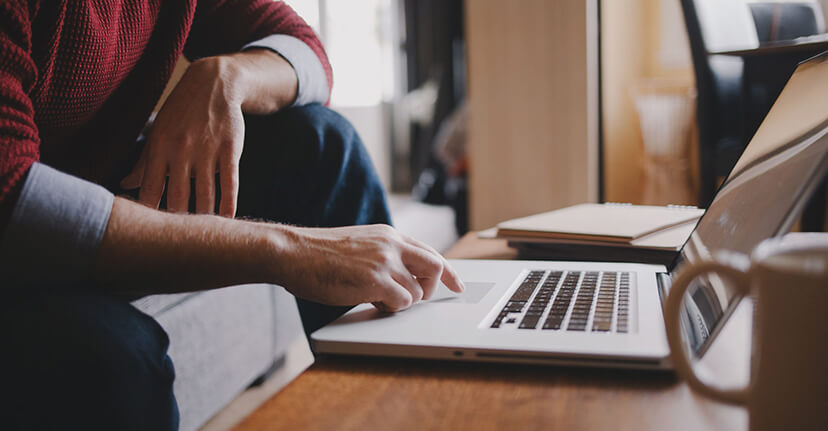 A person sitting at a wooden desk at home, using a laptop to check a student loan servicer account.